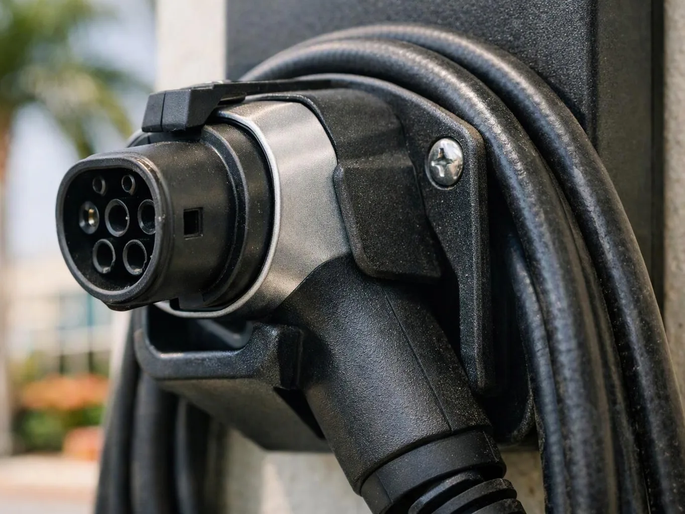 Close-up of an electric vehicle charging plug clipped to a station with a thick cable wrapped around it