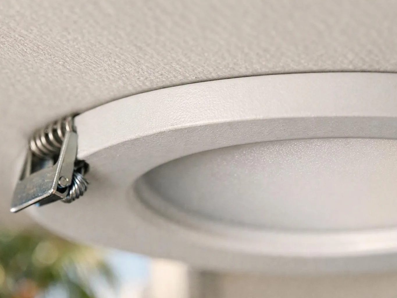 Close-up of a round recessed ceiling light with a metal spring clip and white trim