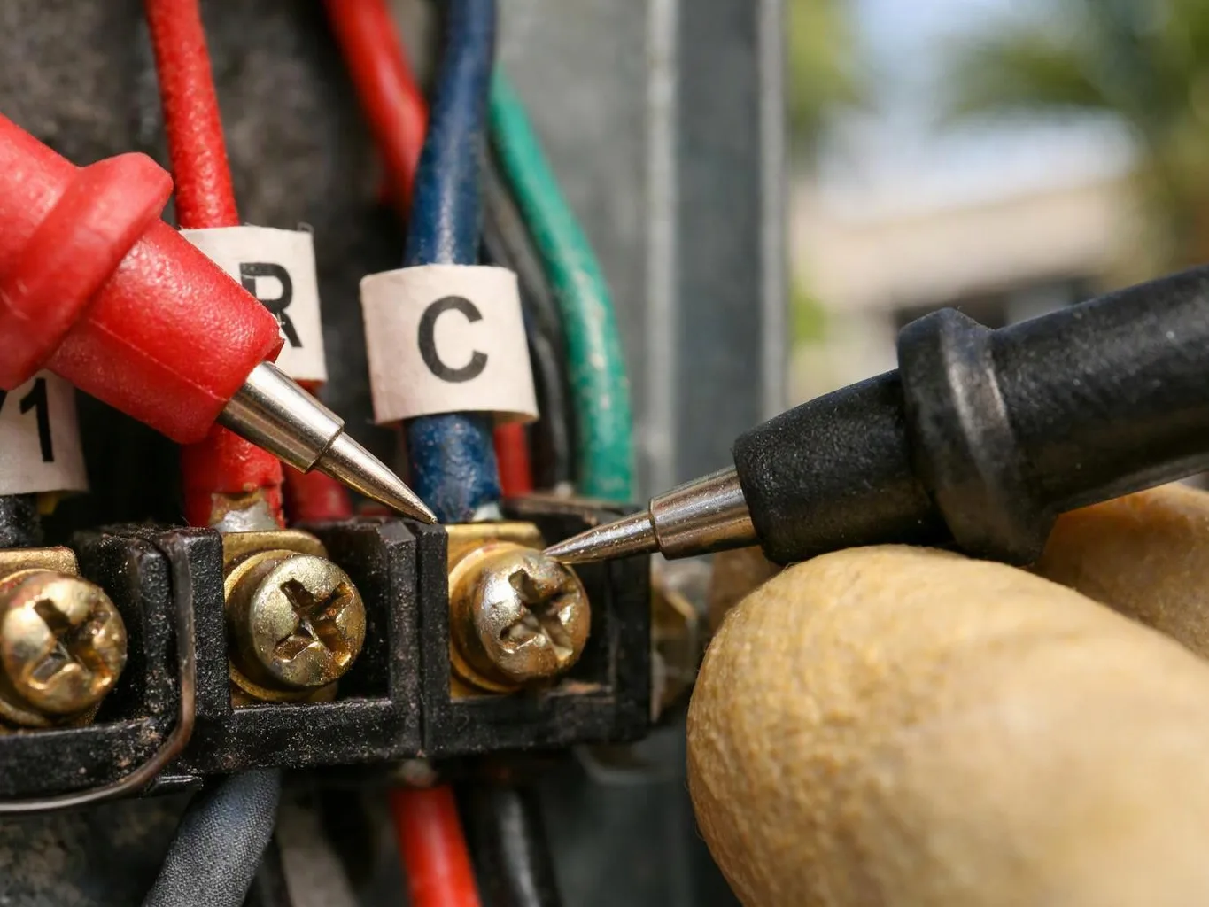 Close-up of test probes touching screw terminals on a color-coded electrical connector block